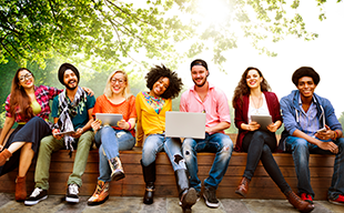 culturally diverse group of millennials sitting outside with laptops