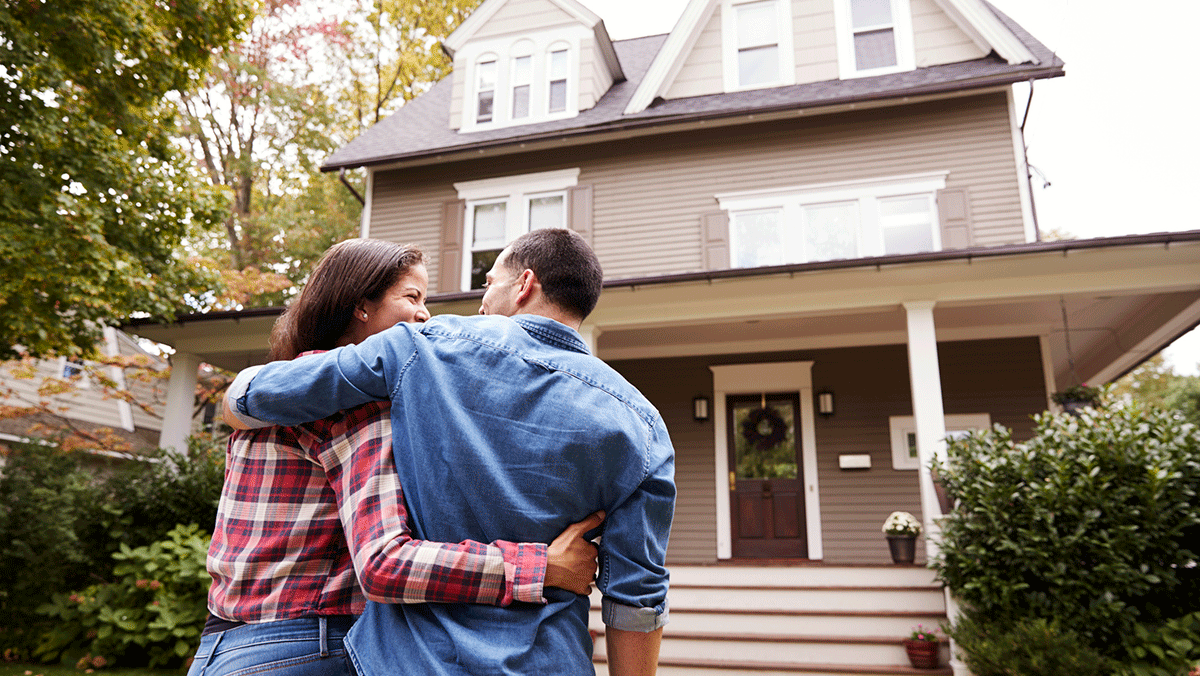 man and woman with arms around each other looking at their new home
